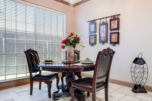 A dining area with a round table, four chairs, a vase with red flowers, and framed pictures on the wall.
