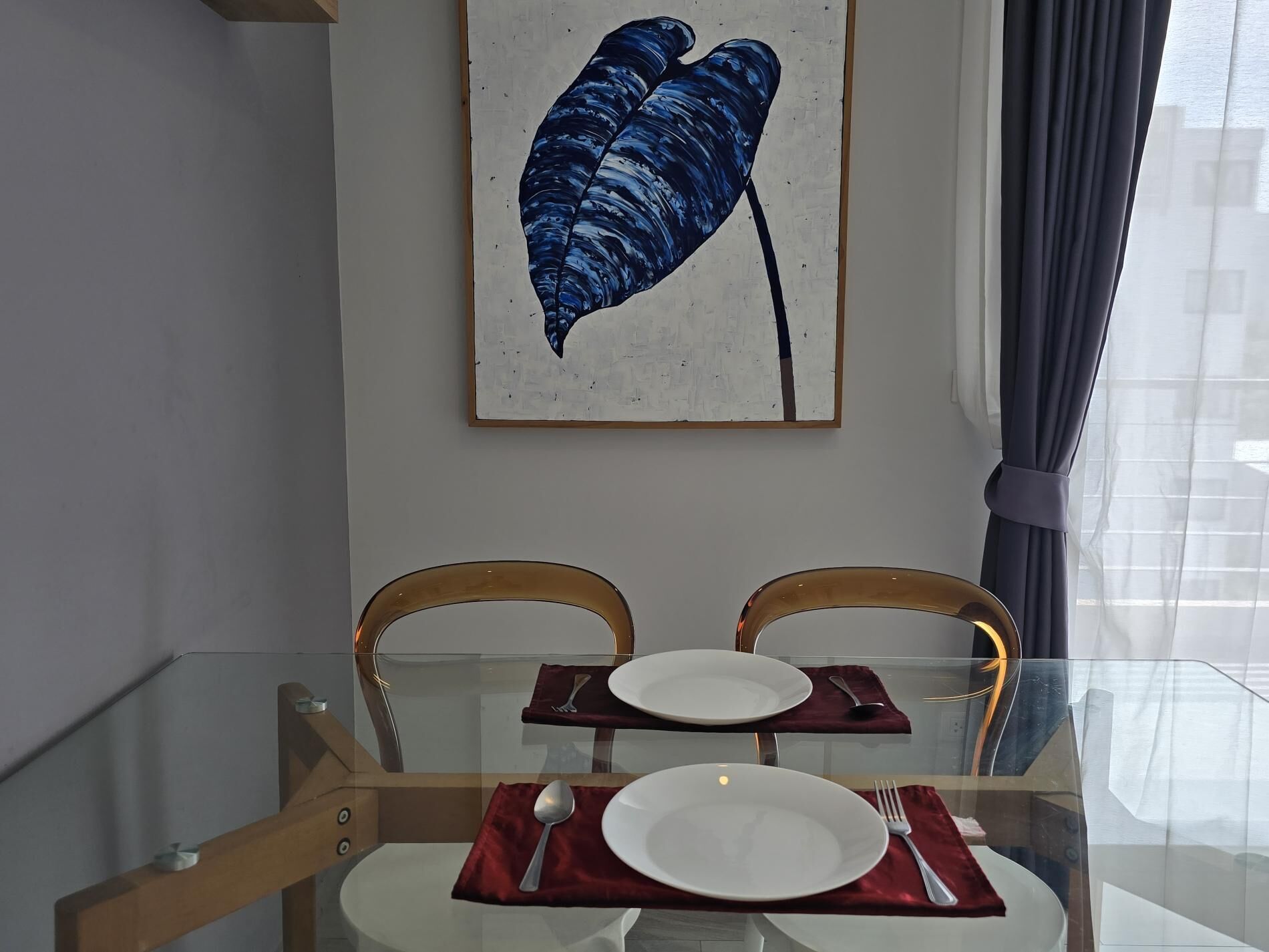 Un comedor con una mesa de vidrio, dos sillas y un cuadro en la pared.