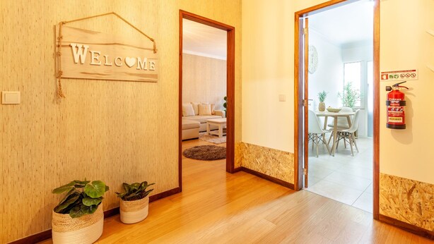 A wooden interior with a 'WELCOME' sign, a fire extinguisher, and a dining area visible through an open door. - Apartamento Hibiscos - Minho s Guest (Braga)