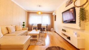 A modern living room with a sofa, coffee table, TV, and dining area. - Apartamento Hibiscos - Minho s Guest (Braga)