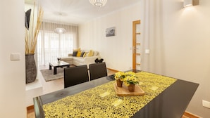 A modern dining area with a black table, yellow patterned table runner, and two potted plants.