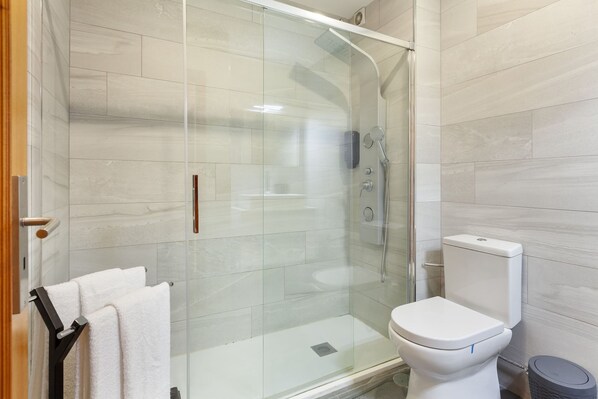 A modern bathroom with a glass-enclosed shower, a white toilet, and a towel rack with white towels.