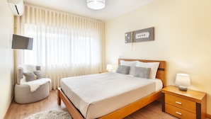 A bedroom with a bed, bedside tables, a chair, a TV, and a window with curtains.