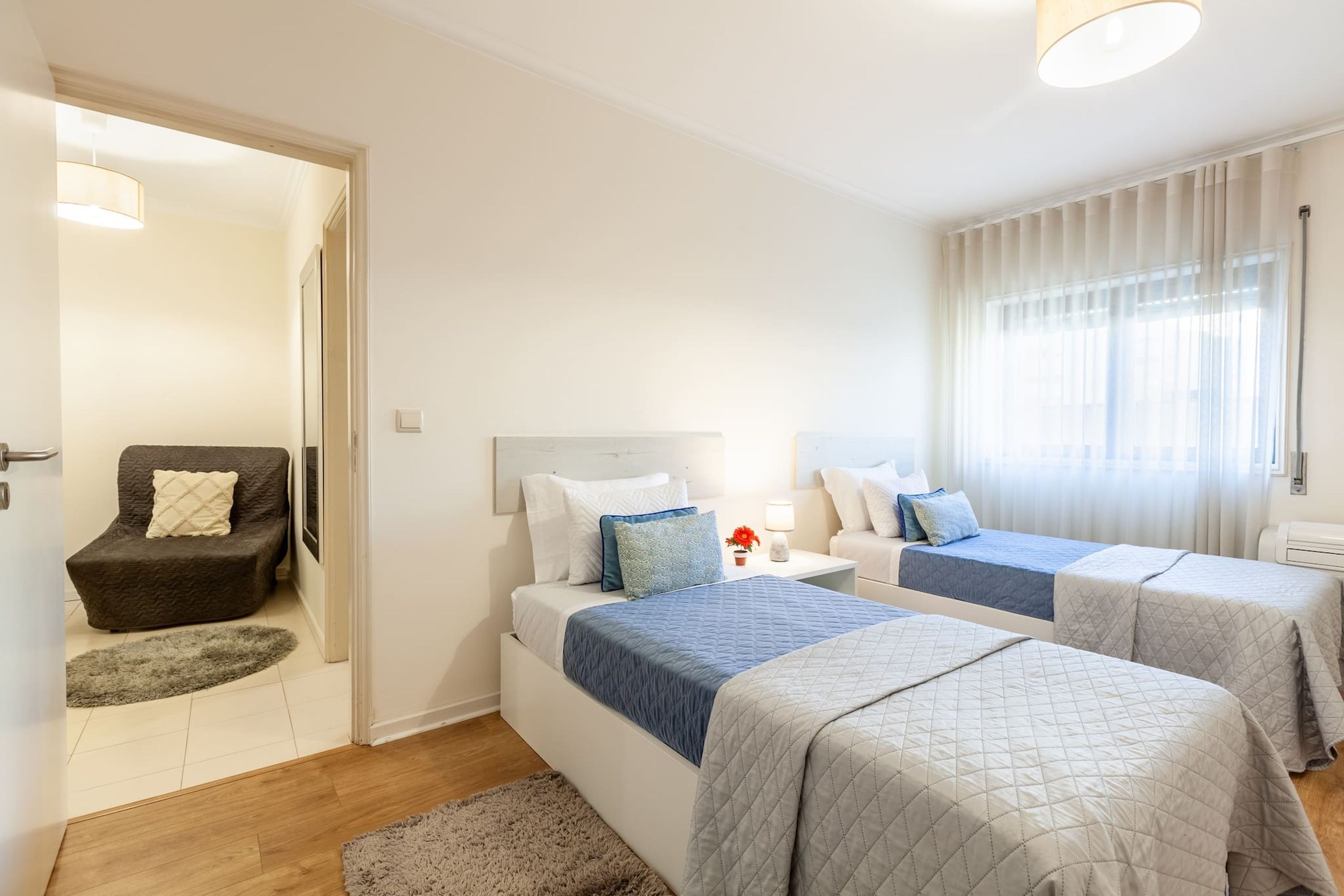 Una camera d'albergo moderna con due letti, un piccolo angolo salotto e un'ampia finestra con tende.