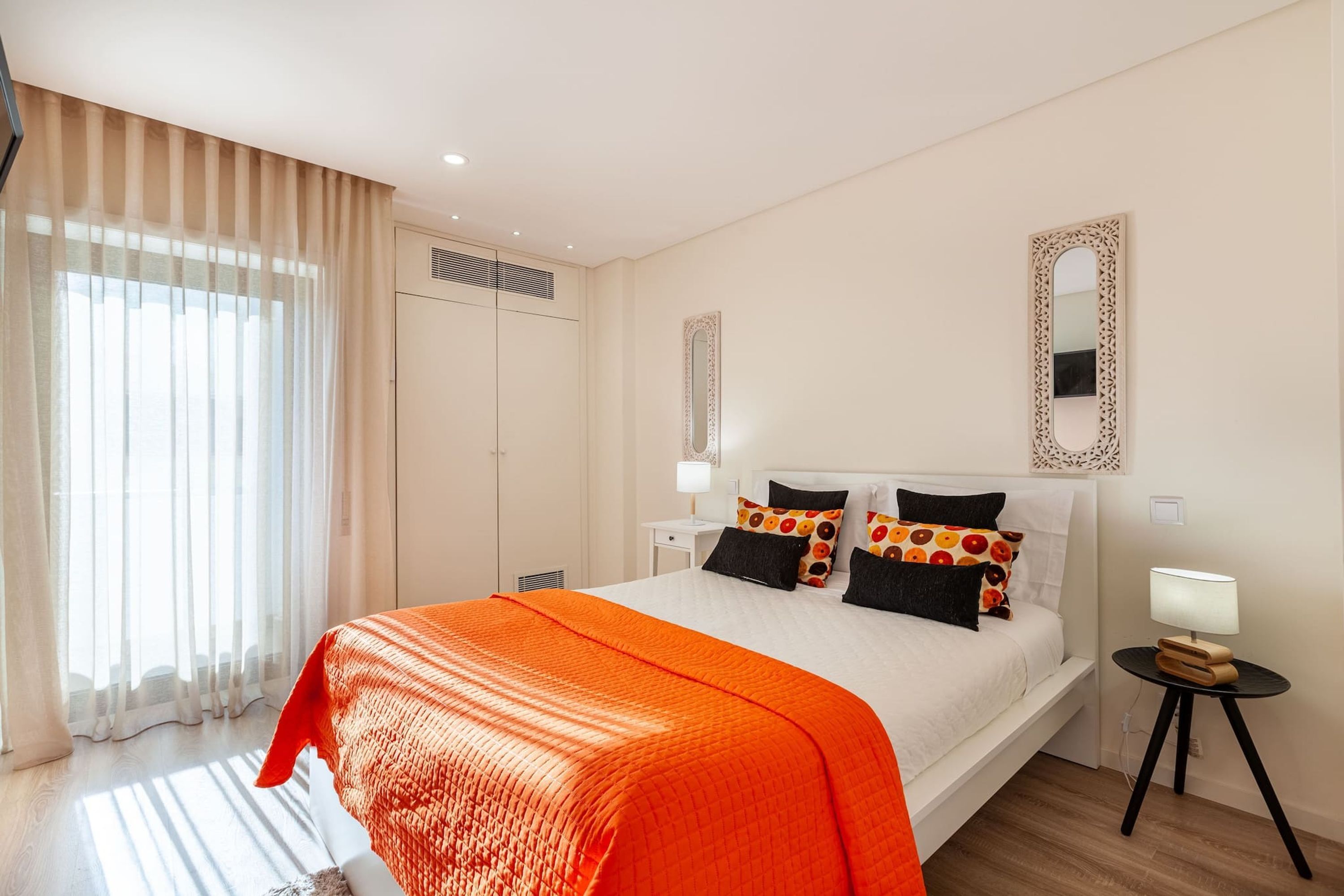 A hotel room with a large bed, a bedside table with a lamp, a wardrobe, and a window with curtains.