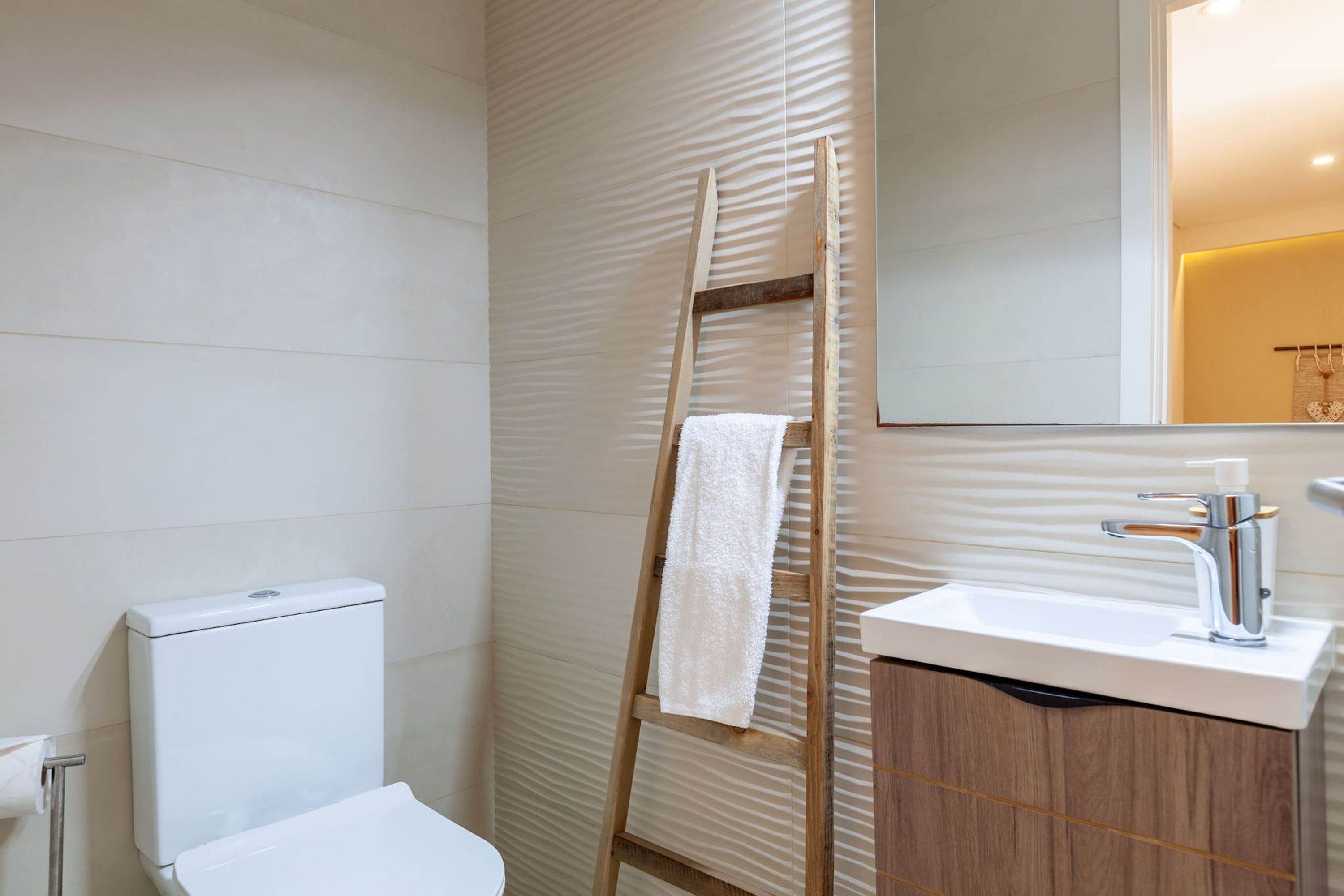 A bathroom with a white toilet, wooden vanity, and a towel on a wooden ladder.