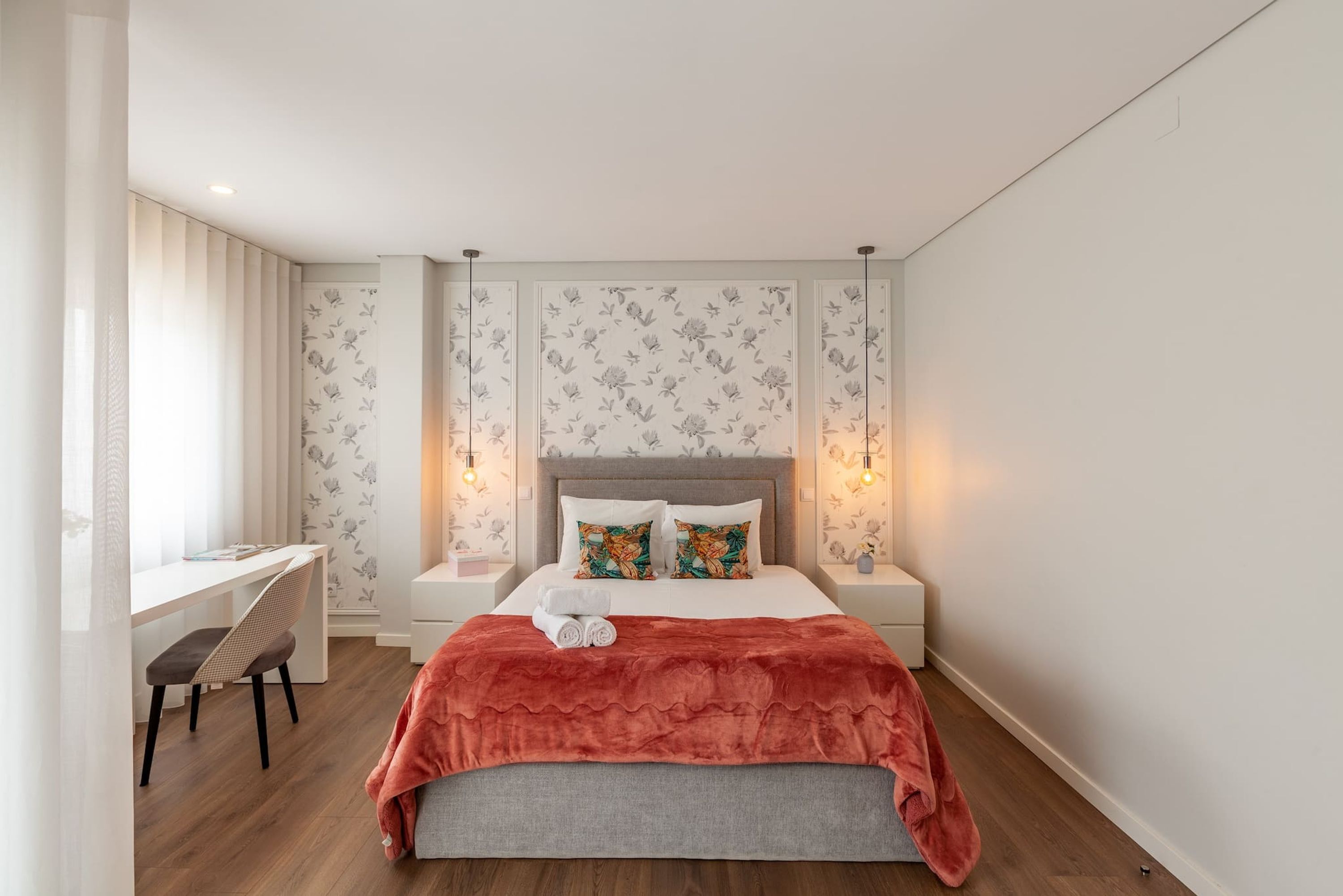 A modern bedroom with a bed, bedside tables, a desk, and a chair.