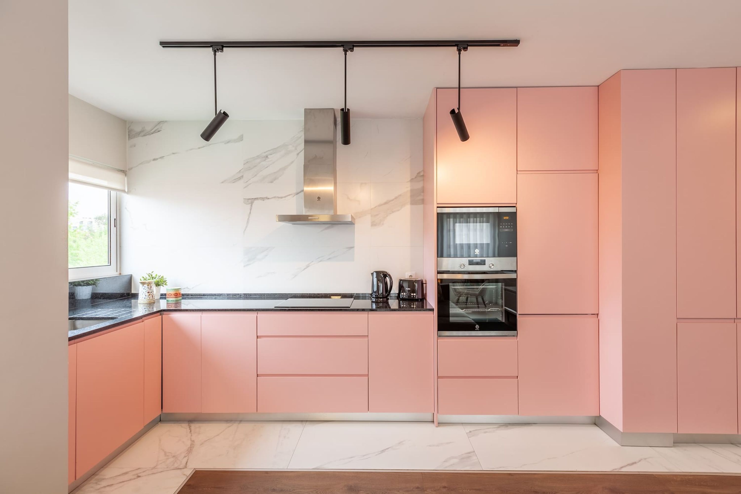 A modern kitchen with pink cabinets, a marble backsplash, and a built-in oven.