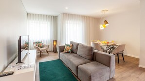 Een moderne woonkamer met een grijze bank, een eettafel met stoelen en een televisie op een witte dressoir.