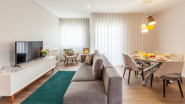Een moderne woonkamer met een flatscreen televisie, bank, eettafel en stoelen.