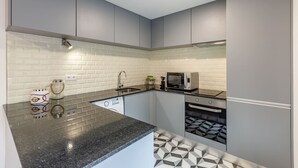 Une cuisine moderne avec des meubles gris, un plan de travail noir, un four à micro-ondes, un lave-vaisselle et un crédence décorée.
