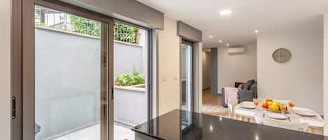 A modern kitchen with a black countertop, a dining area with a table set for two, and a sliding glass door leading to an outdoor area with plants.
