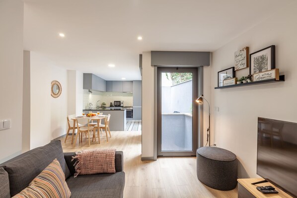 Un salon moderne avec un canapé gris, un pouf rond et un téléviseur à écran plat.
