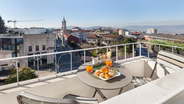 Un balcone con tavolo apparecchiato per la colazione, vista su una città con edifici e una catena montuosa in lontananza.