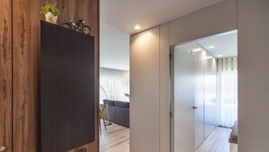 Un interno moderno con una parete in legno decorativa, un mobile scuro e una porta in vetro che dà su un ambiente con un divano e una pianta.