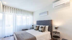 Una camera da letto moderna con un letto grande, una testiera grigia, un comodino con una lampada e un condizionatore d'aria a parete.