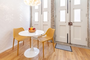 Una habitación con una mesa redonda blanca, dos sillas amarillas, un frutero y una puerta blanca con ventanas.