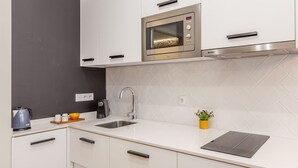 Cocina moderna con armarios blancos, horno de acero inoxidable, un lavamanos y una pequeña encimera con un hervidor y una planta.