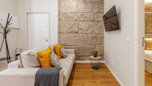 Una sala de estar moderna con una pared de acento de piedra, un sofá con cojines estampados, una pequeña mesita auxiliar y un televisor de pantalla plana montado en la pared.