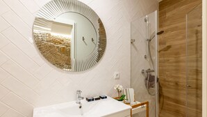 Un baño con pared de azulejos blancos, un espejo redondo, un lavabo blanco y una zona de ducha.