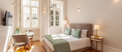 A bedroom with a bed, bedside table, lamp, chair, and a small table with a plant and glasses.