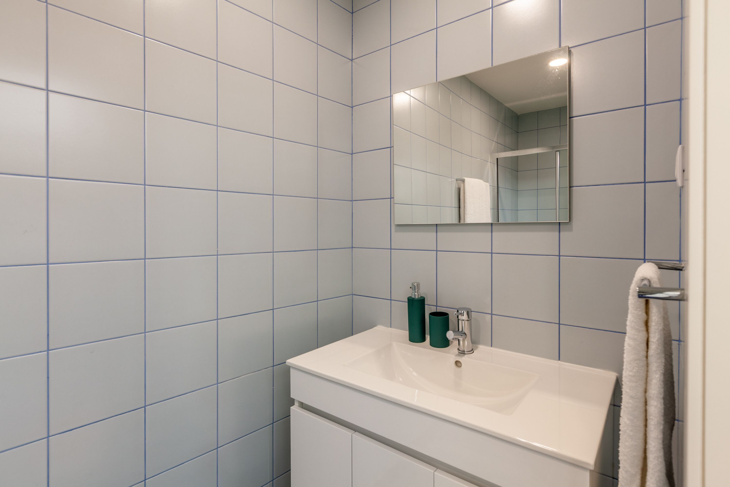 Un bagno con pareti in piastrelle blu, un lavandino bianco, uno specchio e un asciugamano appeso al muro.