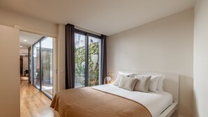 Ein modernes Schlafzimmer mit einem großen Bett, einer Glastür, die auf einen Balkon führt, und Holzboden.