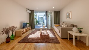 Ein modernes Wohnzimmer mit einer Couch, einem Couchtisch, einem Fernseher und Blick durch eine Glastür in einen Außenbereich.