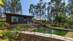 Una casa moderna con un muro de piedra, una terraza de madera y un estanque.