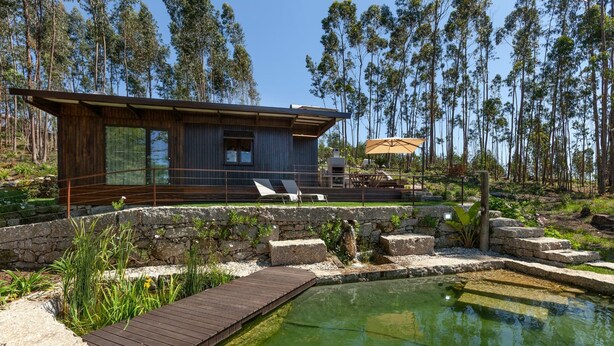 Una cabaña moderna con terraza, piscina y un muro de piedra.