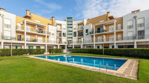 Un moderno edificio residenziale con piscina centrale, circondato da prati curati e siepi.