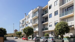 Filare di edifici residenziali moderni con balconi, una strada acciottolata e auto parcheggiate.