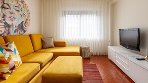 Un soggiorno moderno con un divano, un poggiapiedi e una TV a schermo piatto su un mobile bianco.
