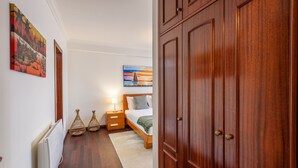Una camera da letto con un armadio in legno, un letto con copripiumino bianco, un comodino con lampada e due quadri appesi al muro.