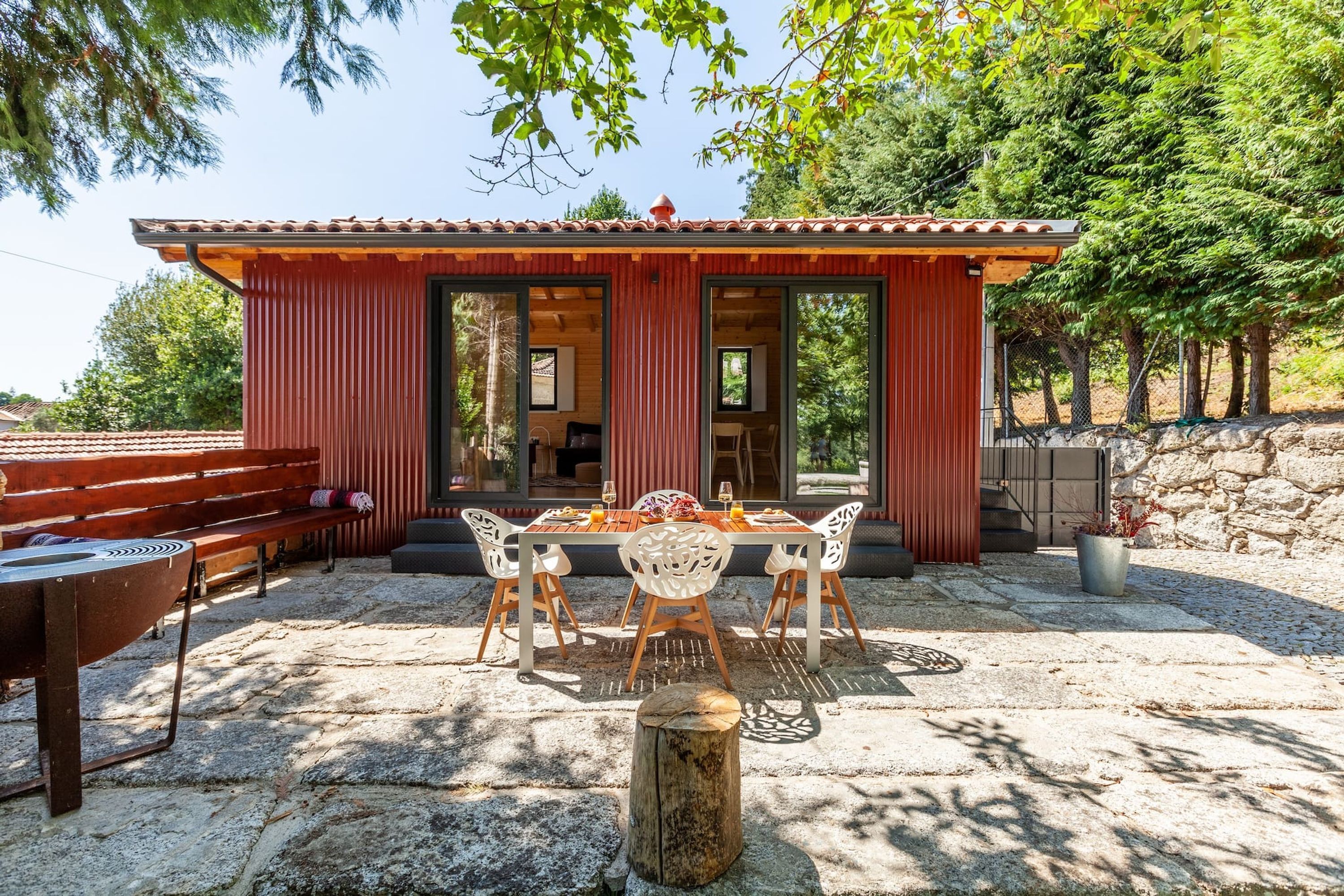 A wooden cabin with a dining area featuring a table and chairs, a bench, and a grill outside.
