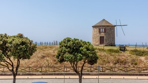Una torre de piedra con un molino de viento sobre una colina cubierta de hierba, cerca de una carretera costera.