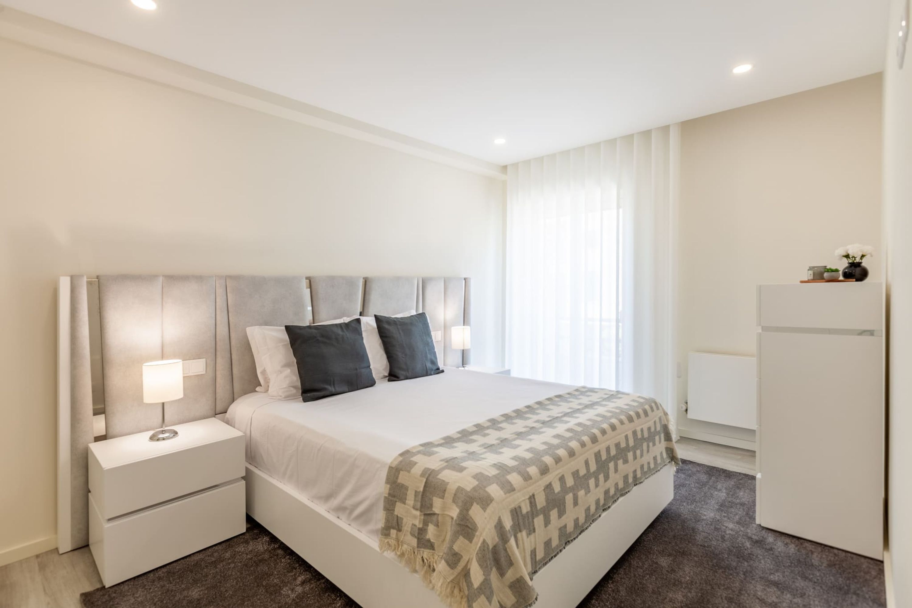 A modern bedroom with a large bed, bedside tables, a nightstand, a dresser, and a built-in wardrobe.