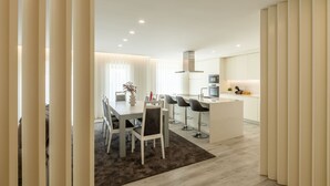 Una cocina moderna con una isla central, un comedor con mesa y sillas, y un gran ventanal con cortinas.