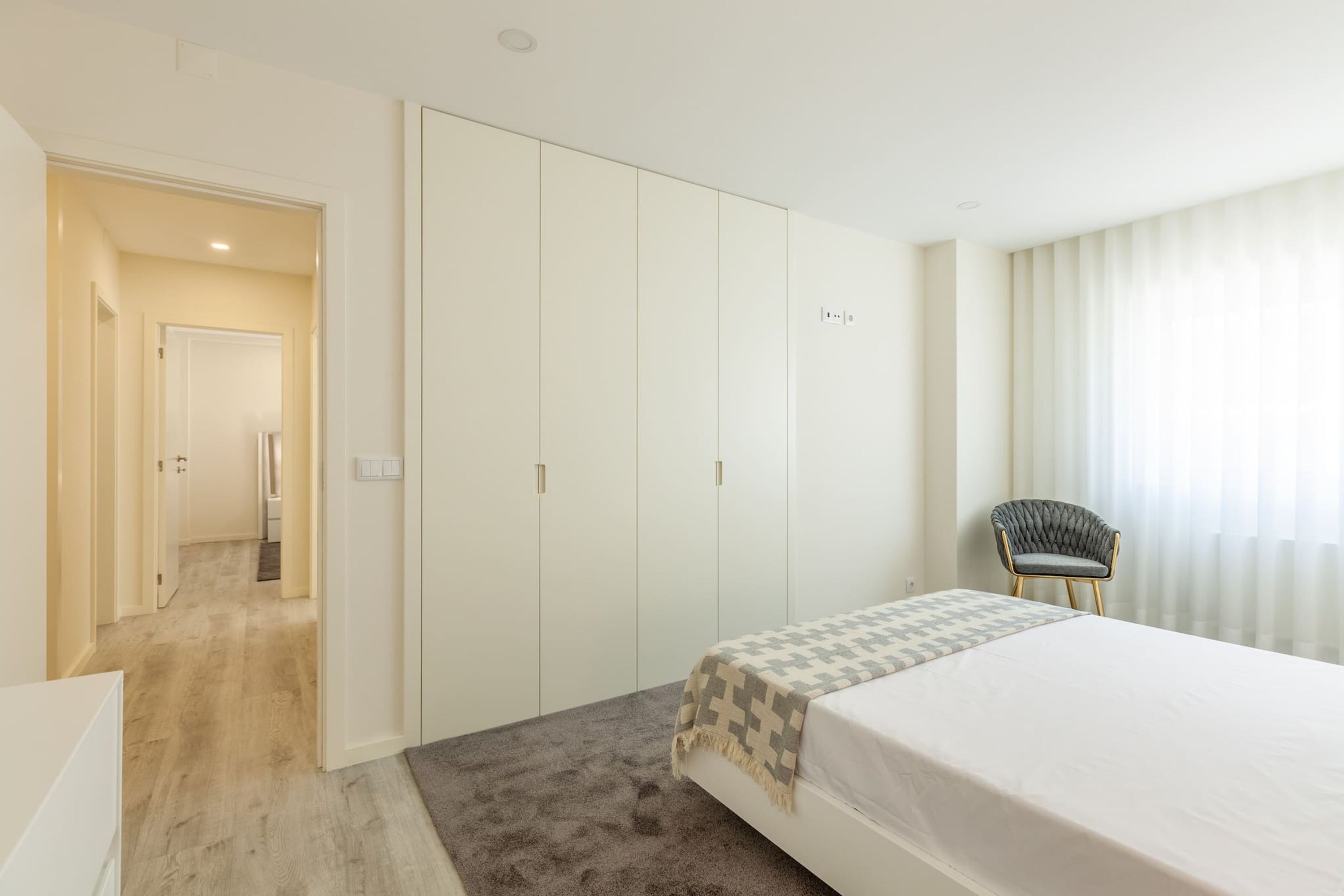 Ein Schlafzimmer mit Bett, Kleiderschrank, Stuhl und einem Badezimmer im Hintergrund.