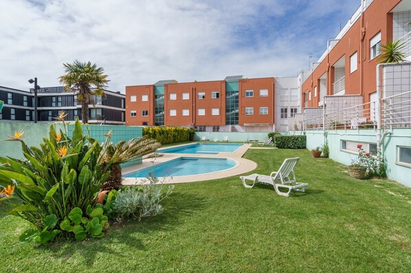 A swimming pool surrounded by a well-maintained lawn, with a building in the background. - Ofir Beach Lodge By Minho s Guest (Esposende)