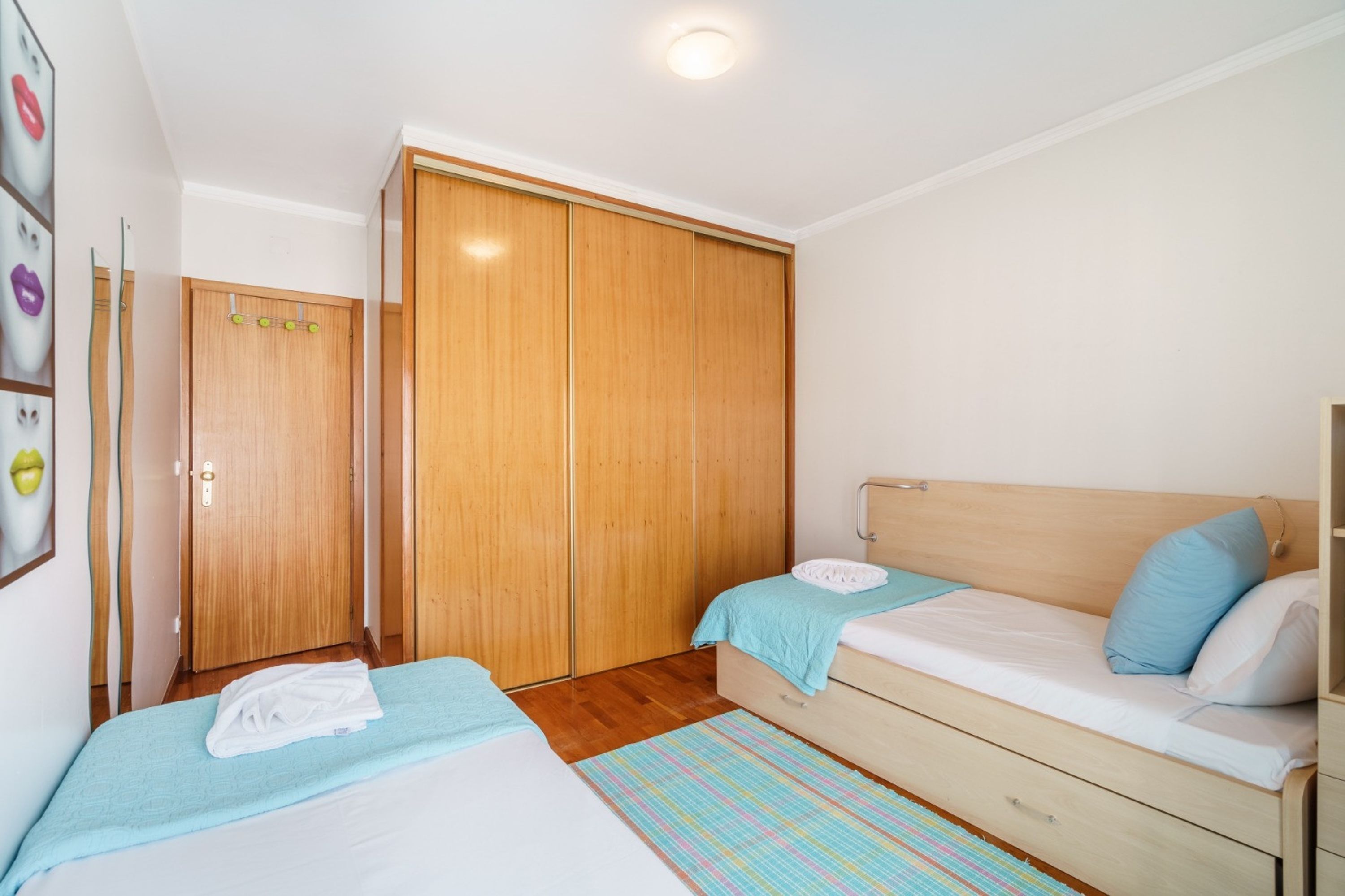 Quarto com duas camas, um guarda-roupa de madeira e um banheiro pequeno.