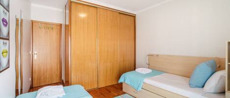 Quarto com duas camas, um guarda-roupa de madeira e um banheiro pequeno.