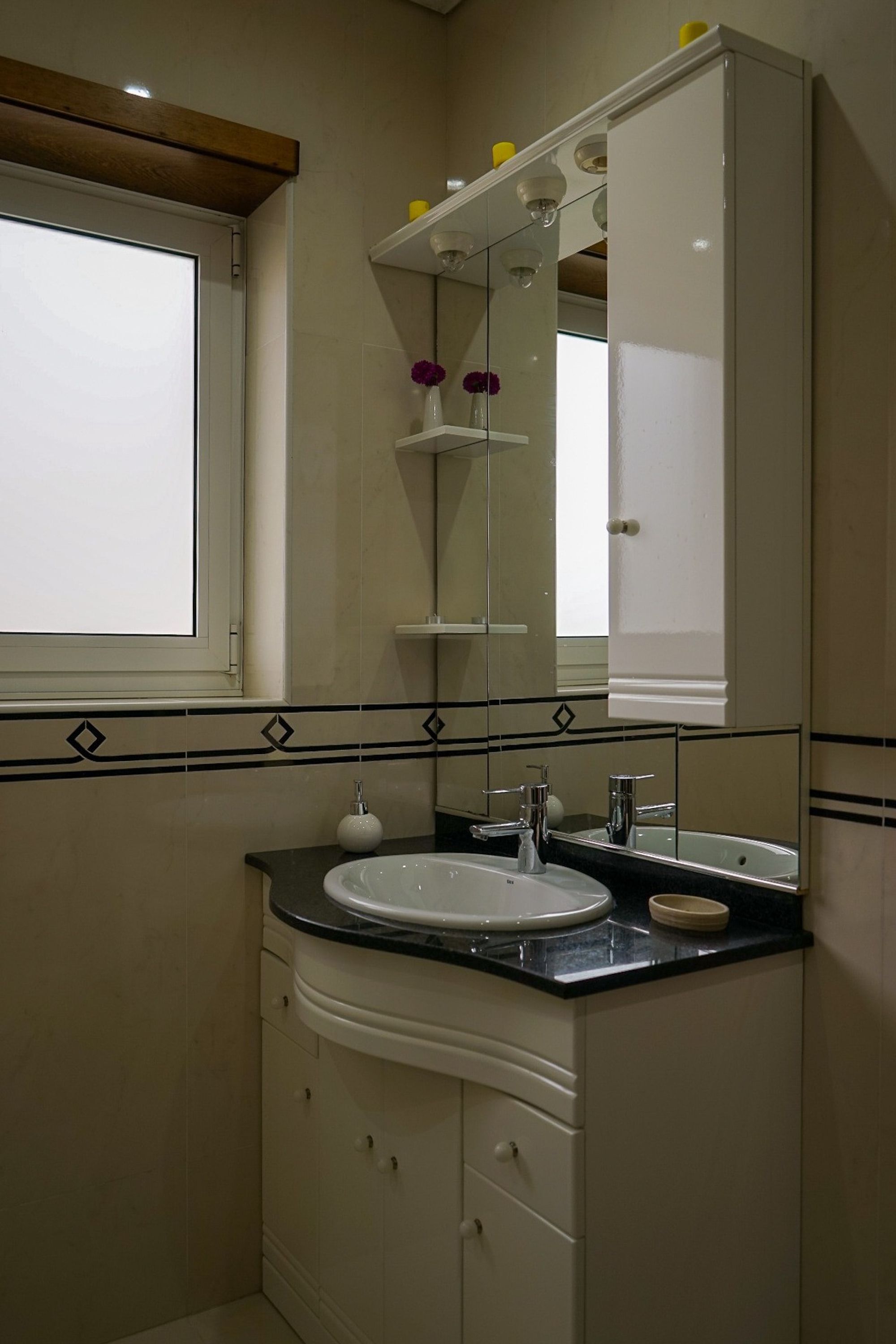 Une salle de bain avec un lavabo blanc, un miroir et une fenêtre.