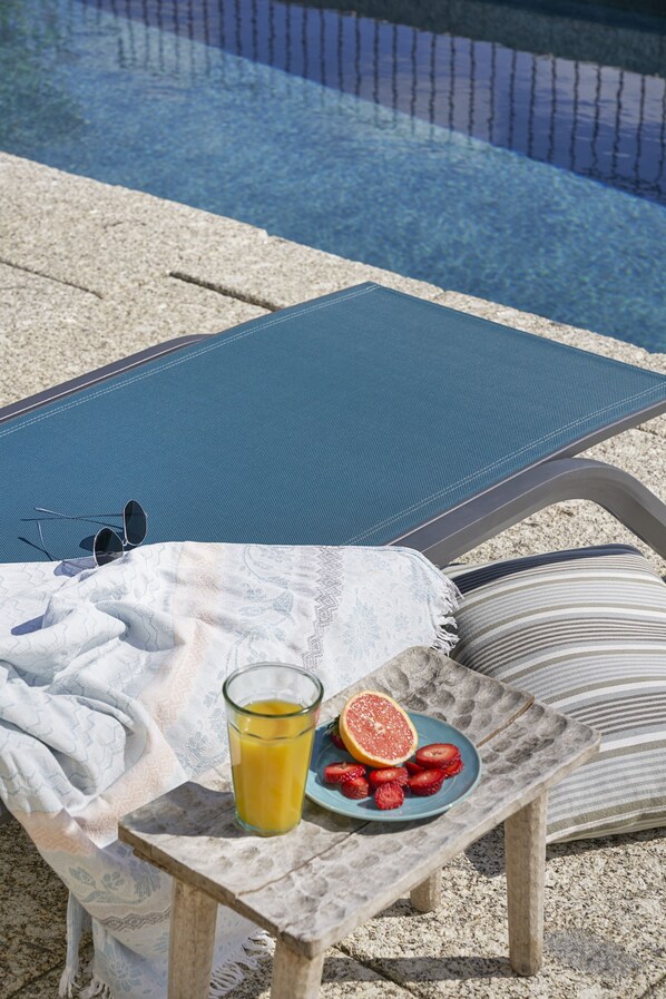 A poolside lounge chair with a table, a glass of orange juice, and a plate of strawberries and a grapefruit. - Casa do Xico - Minho s Guest (Guimarães)