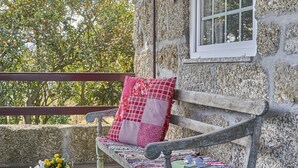 A stone building with a wooden bench, a wicker stool, and a table with a drink. - Casa do Xico - Minho s Guest (Guimarães)