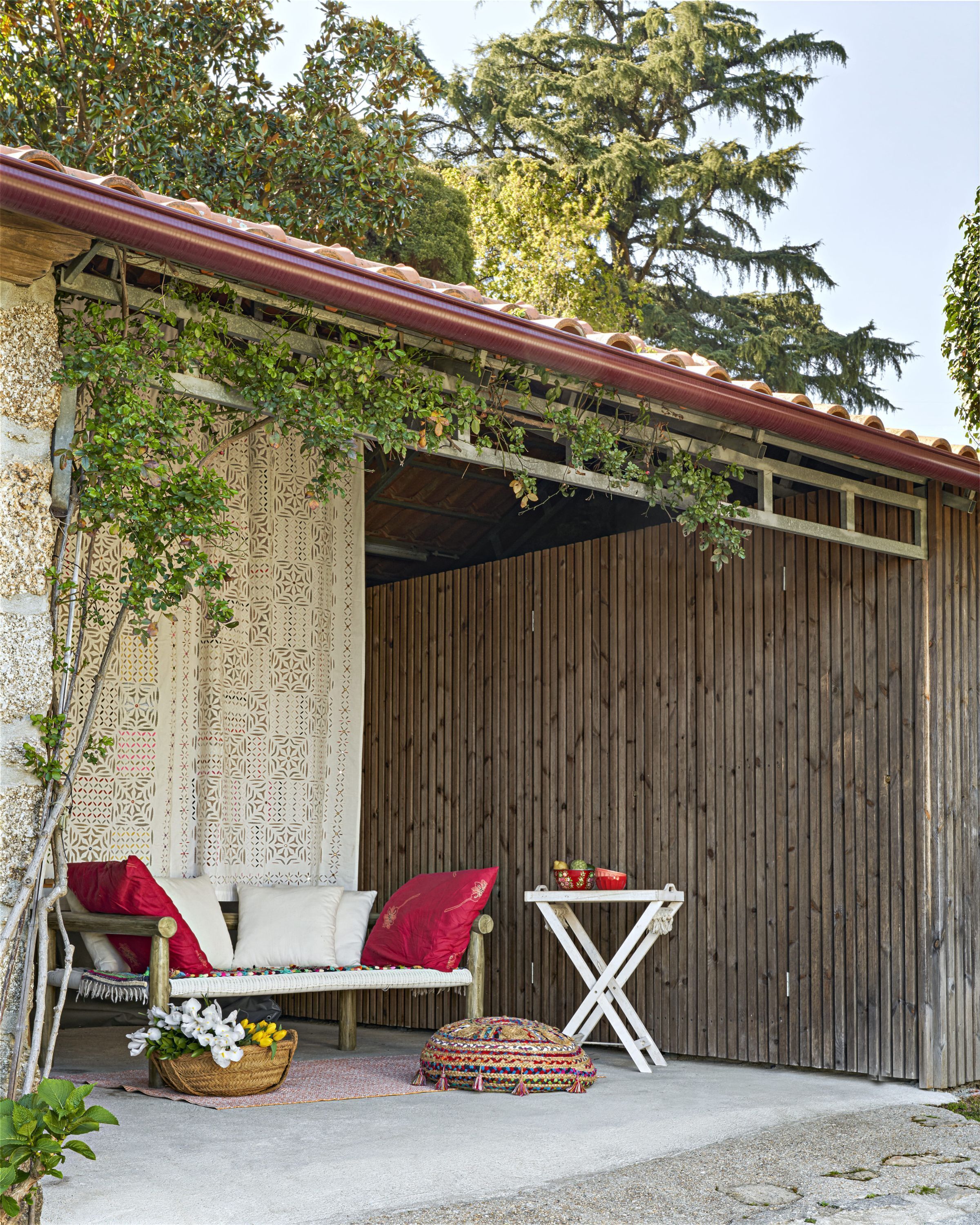 A cozy outdoor seating area with a wooden bench, cushions, and a woven basket with flowers.