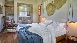A bedroom with a bed, wooden floor, stone wall, and a hanging light fixture. - Casa do Xico - Minho s Guest (Guimarães)
