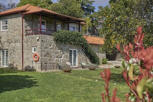 Un edificio de piedra con techo de tejas rojas, un balcón y un patio césped con cerca.