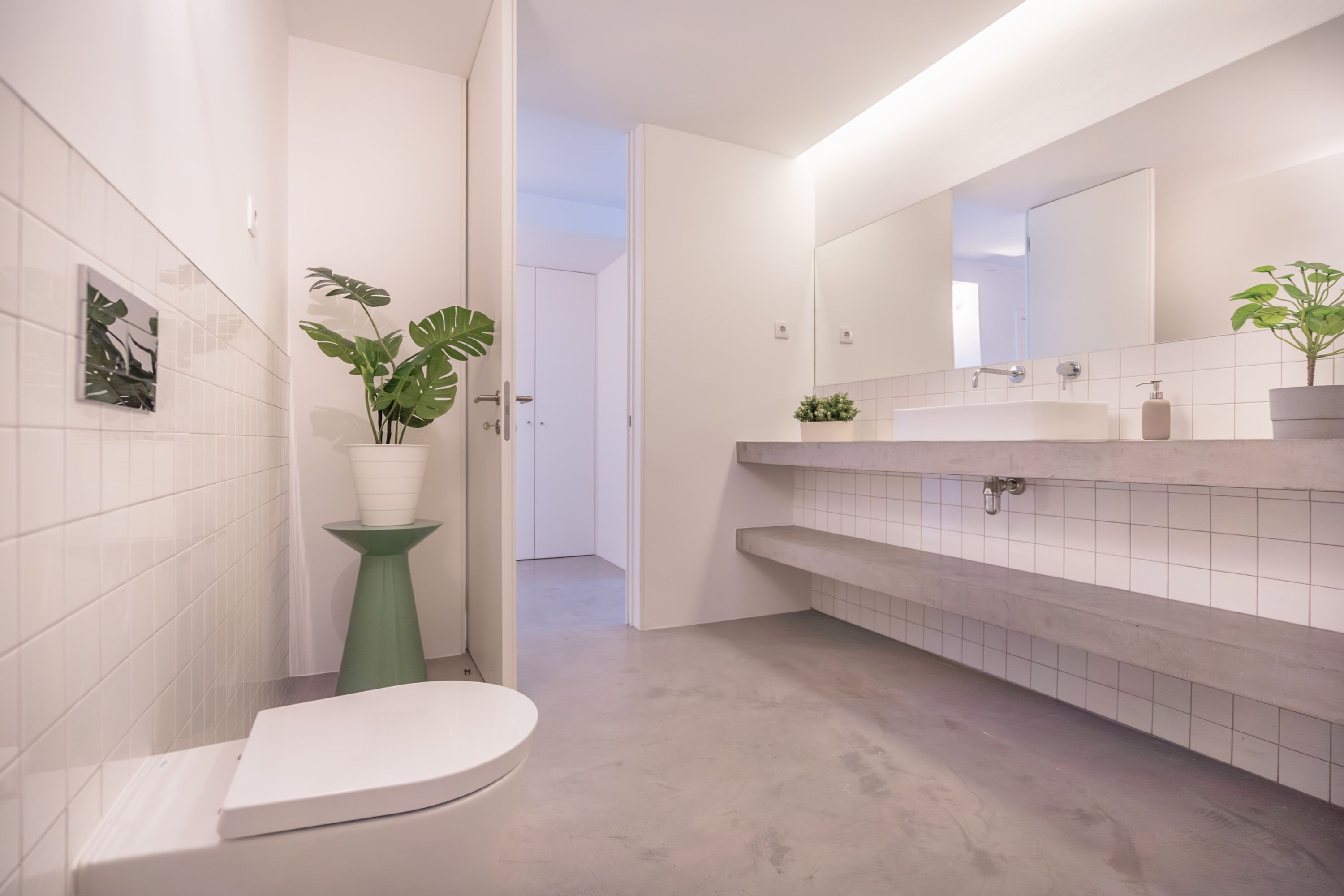 Un baño moderno con inodoro blanco, lavabo pedestal verde y un espejo grande sobre el mueble.
