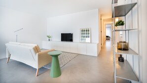 Un soggiorno moderno con un divano, un tavolino rotondo, una TV a schermo piatto e una mensola decorata con oggetti ornamentali.